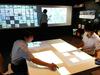 Fujitsu staffers demonstrate a digital brainstorming system in Tokyo on August 6, 2015, sending projected sticky notes from the table to the wall in the background. 